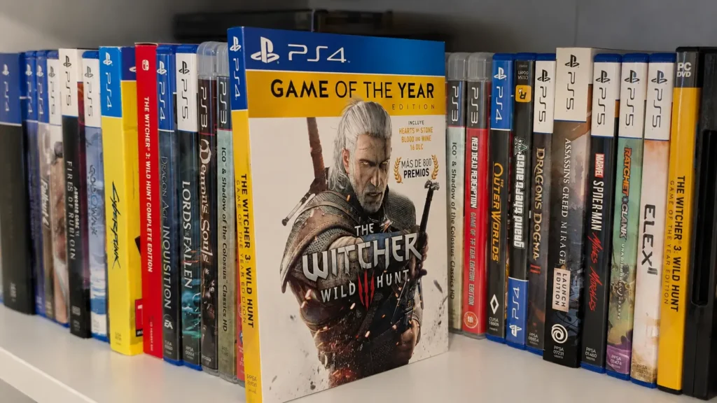 Edición física de The Witcher 3: Wild Hunt para PC delante de una colección de juegos de PlayStation, Nintendo Switch y otras plataformas.